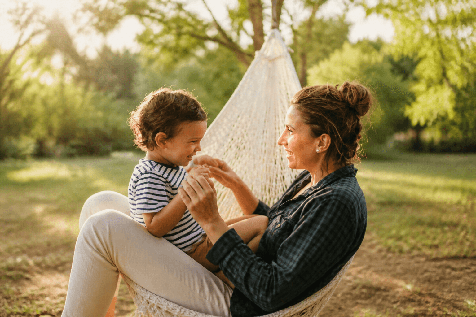 A mother and young child smiling together outdoors in warm sunlight